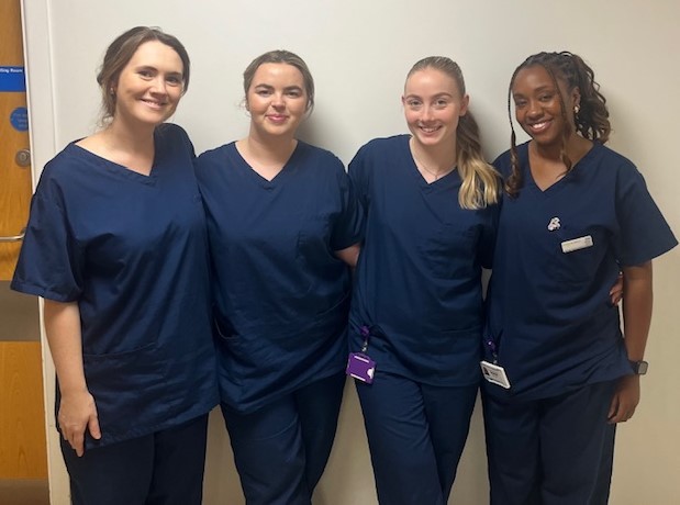 Four members of the physiotherapy team wearing navy blue scrubs stood in a line smiling