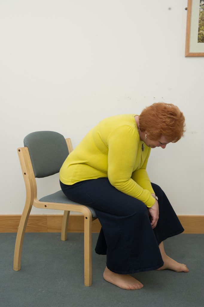 Photograph of a person sat in a chair leaning forward with their arms in between their legs