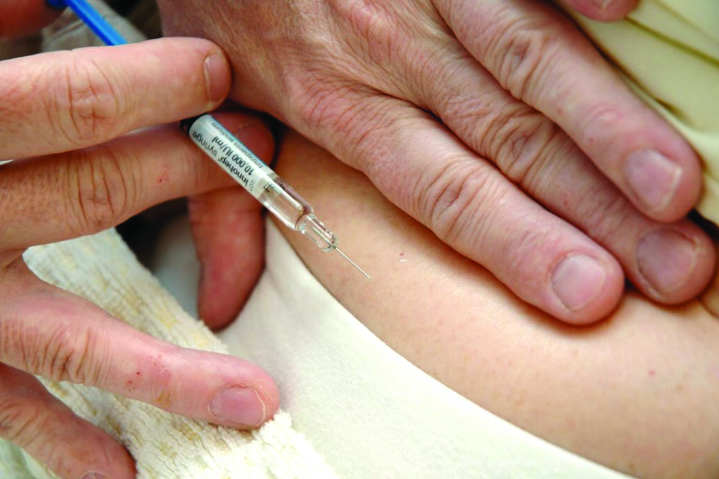 A person’s abdomen is shown while administering a subcutaneous injection with a syringe.