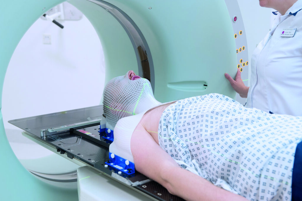A photograph of patient in radiotherapy mask on CT scanner couch.