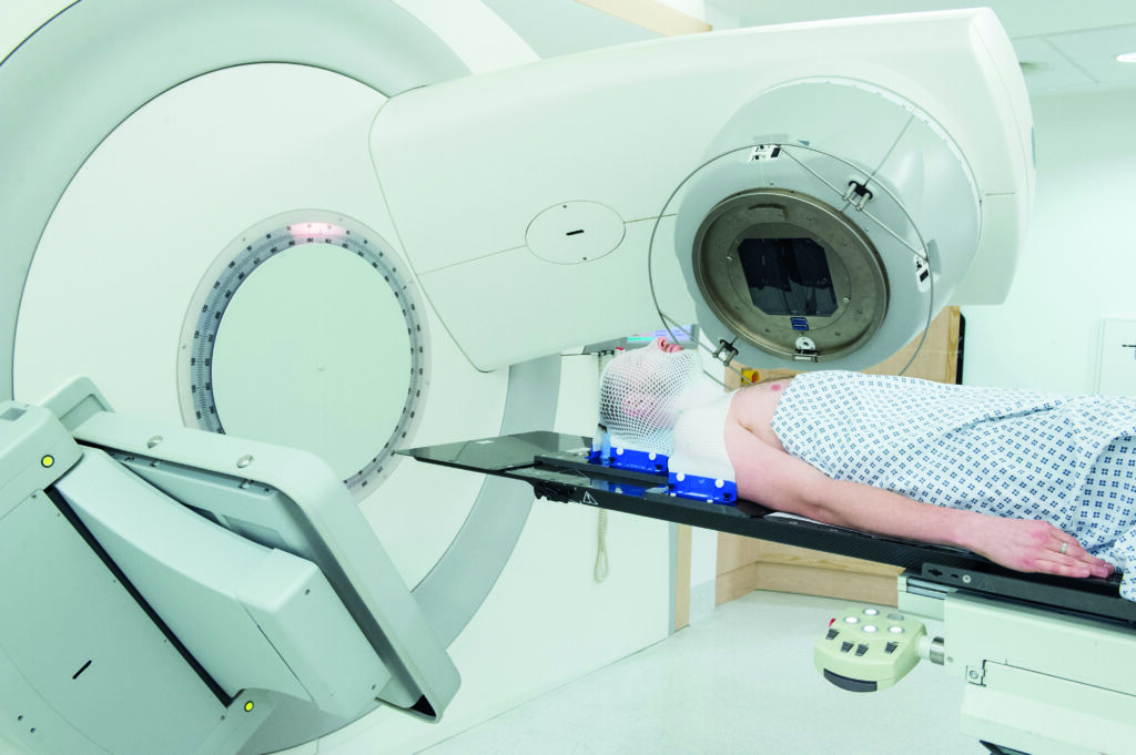 Photograph of a patient in a radiotherapy mask on linear accelerator couch.