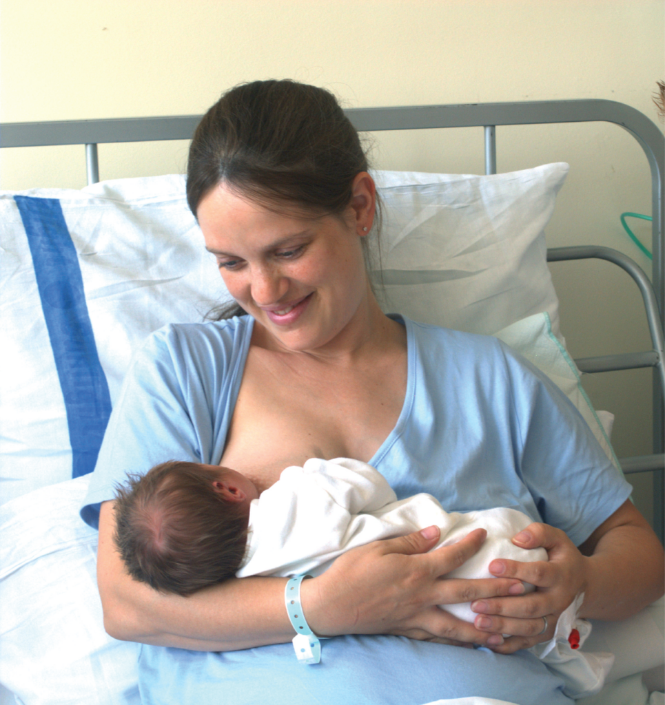 Parent breastfeeding a baby while sitting upright in a hospital bed.