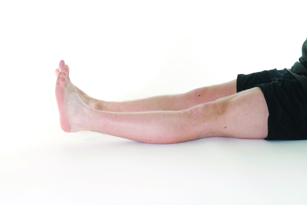 Photograph of a persons legs laying flat with thigh muscles tense