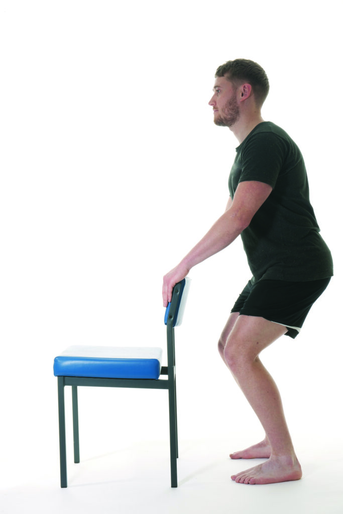 Photograph of a person holding the back of a chair in a squat position