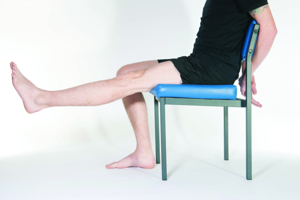 Photograph of a person sat on a chair with one leg relaxed and the other raised upwards