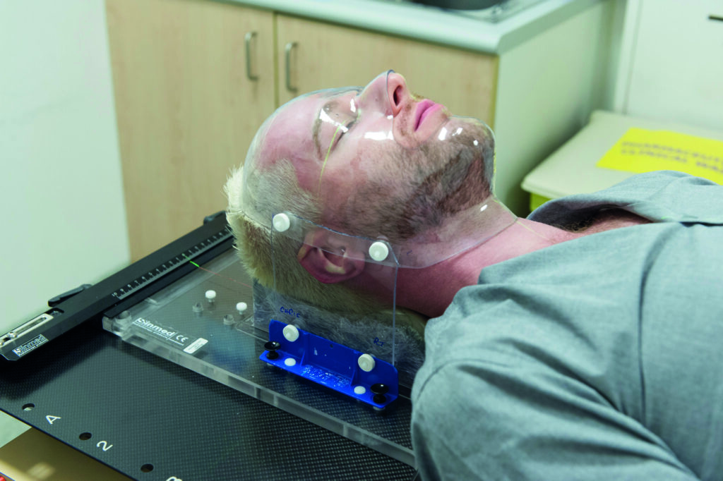 Photograph of a patient on couch, with clear plastic mask fitted to them.