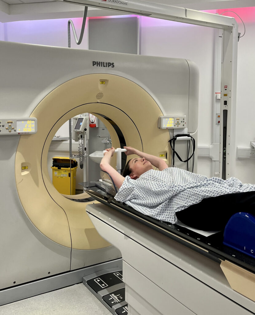 Photograph of a patient lying on scan couch with both arms up as an example of a treatment position.