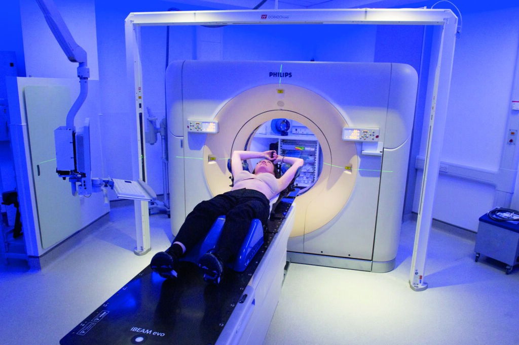 Photograph of a patient on CT couch with both arms up.