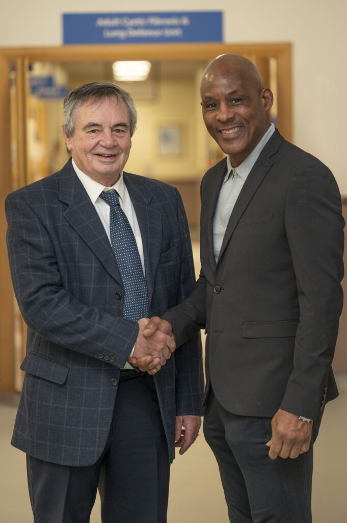 Two men in suits shaking hands in a hospital corridor