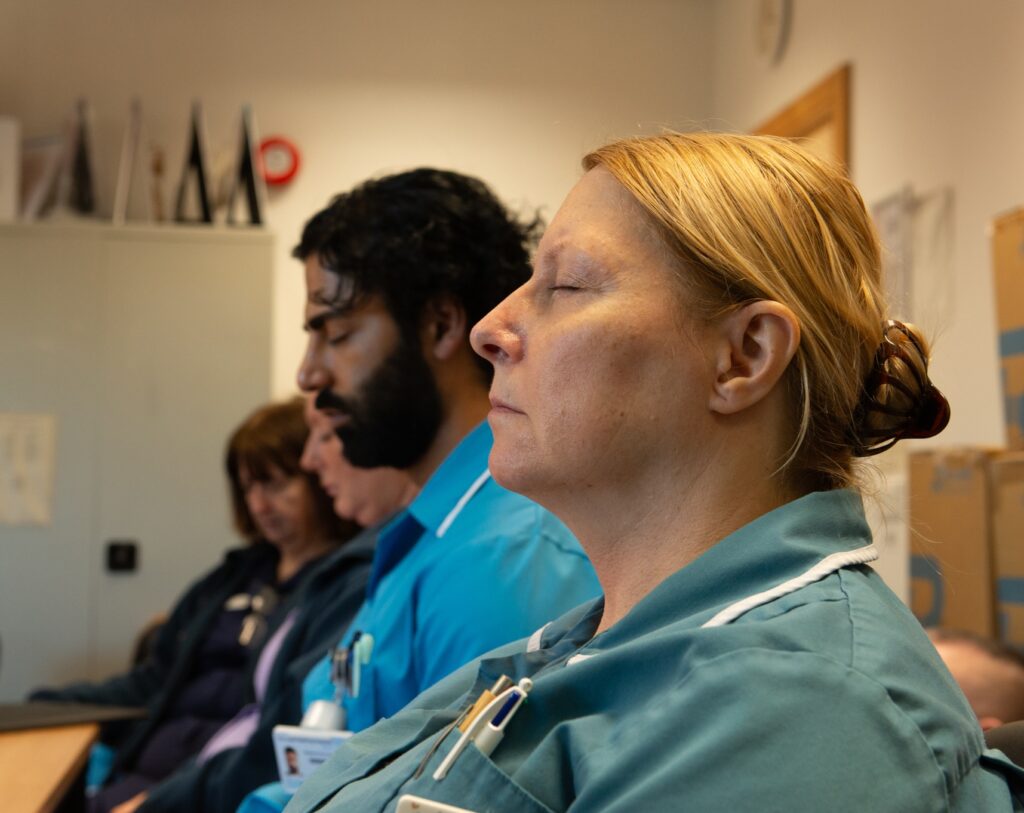 Several people in blue clinical uniforms sat in an office with their eyes closed