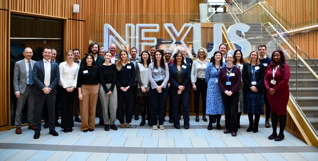 An image of the full visitor group from the HM Treasury and NIHR visit with representatives of the Leeds research community at Leeds Nexus in front of a sign reading 'NEXUS'.