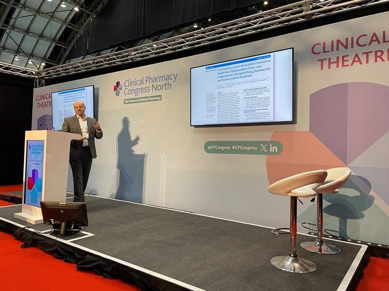 An image showing the InnoMeds Team member Dr Rani Khatib standing on a stage at a lectern undertaking a speech on a PowerPoint Presentation at the Clinical Pharmacy Congress North.