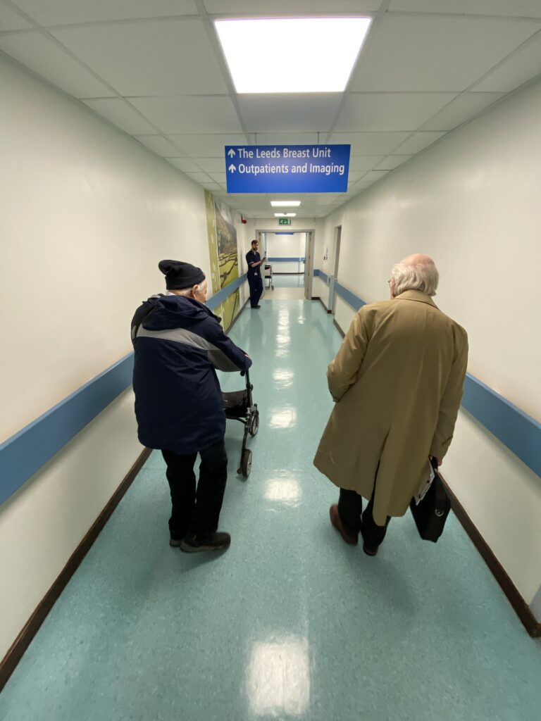 Two people in coats walking down a hospital corridor
