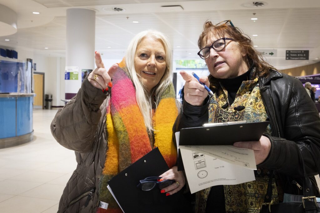 Two people in coats and scarves with a clipboard stood in a hospital lobby