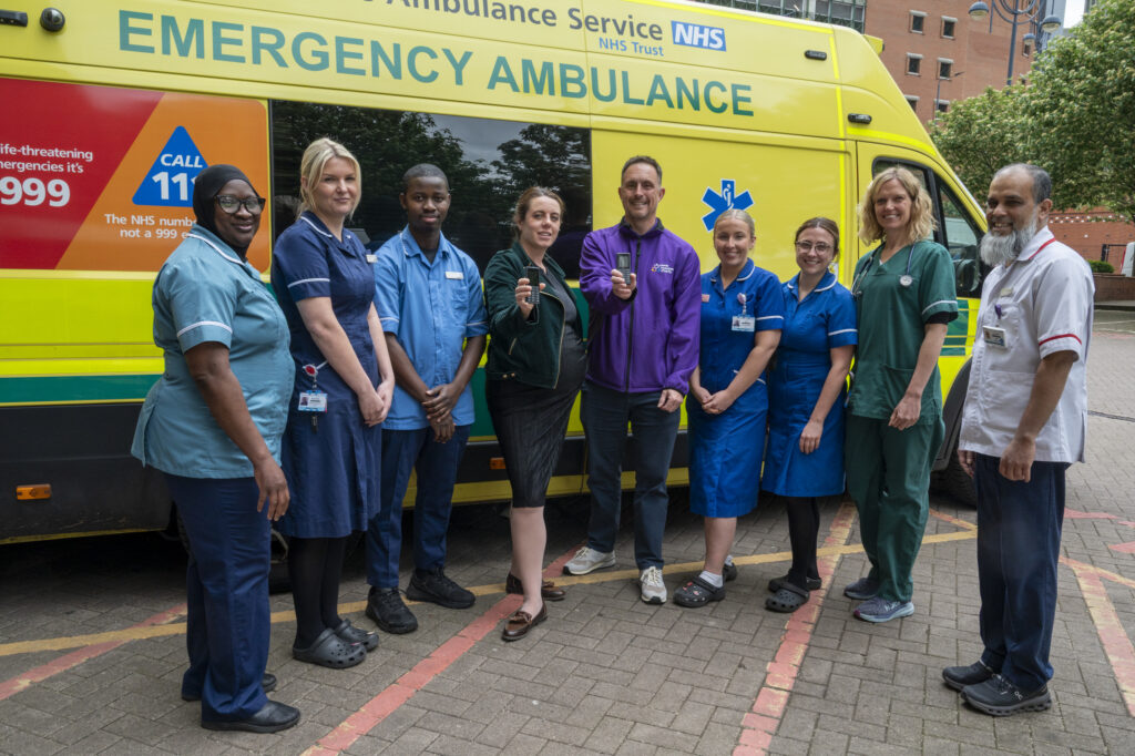A group of people in different coloured clinical uniforms stood in front of an ambulance