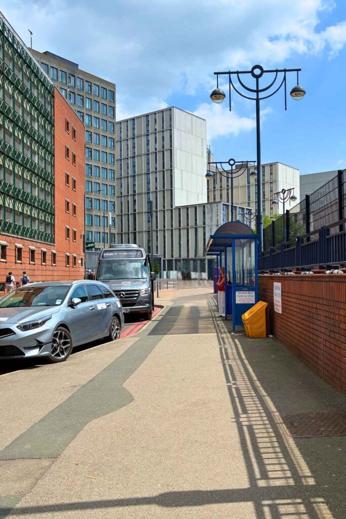 Pavement with blue bus stop on the right and grey car and bus in the layby opposite