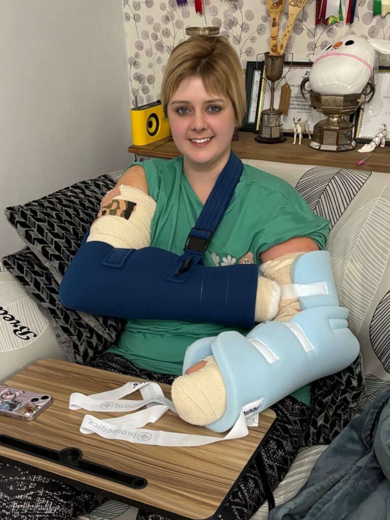 A woman in a green top sat in an armchair with two blue full-length bandages on both arms