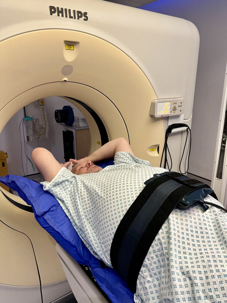 A photograph of a patient wearing an abdominal compression belt whilst lying on a CT couch.