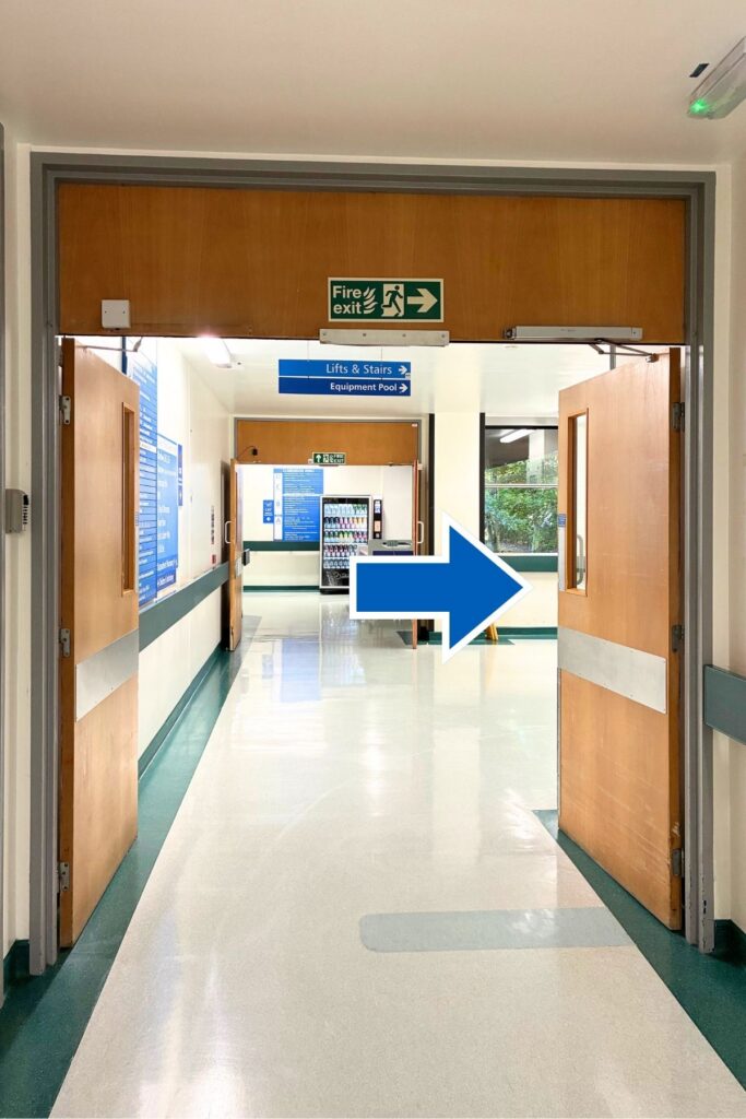 View of open doors at end of corridor, a vending machine and blue arrow pointing to the right