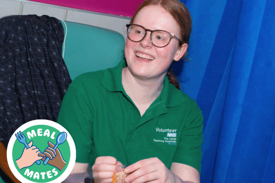 A person in a green volunteer uniform sat next to a blue curtain on a ward
