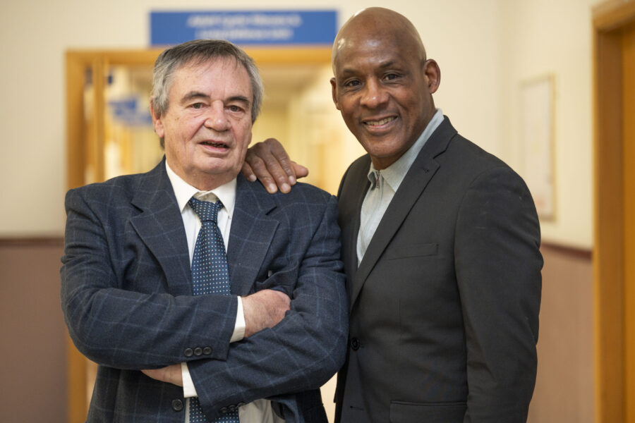 Two men in dark grey suits stood in a hospital corridor