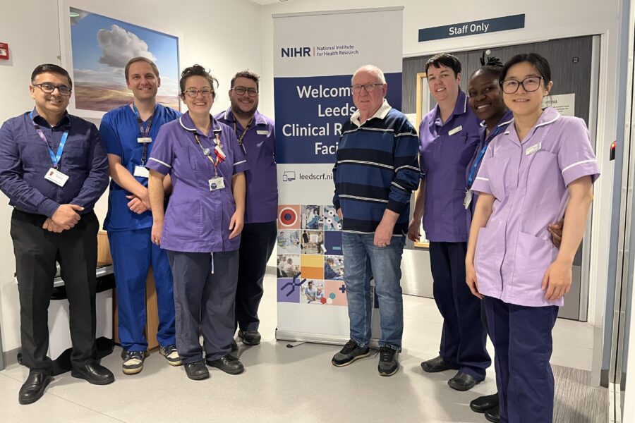 An image of the trial team smiling at the NIHR Leeds Clinical Research Facility with the patient, Mr Phillip Hatton, in front of a banner for the facility.