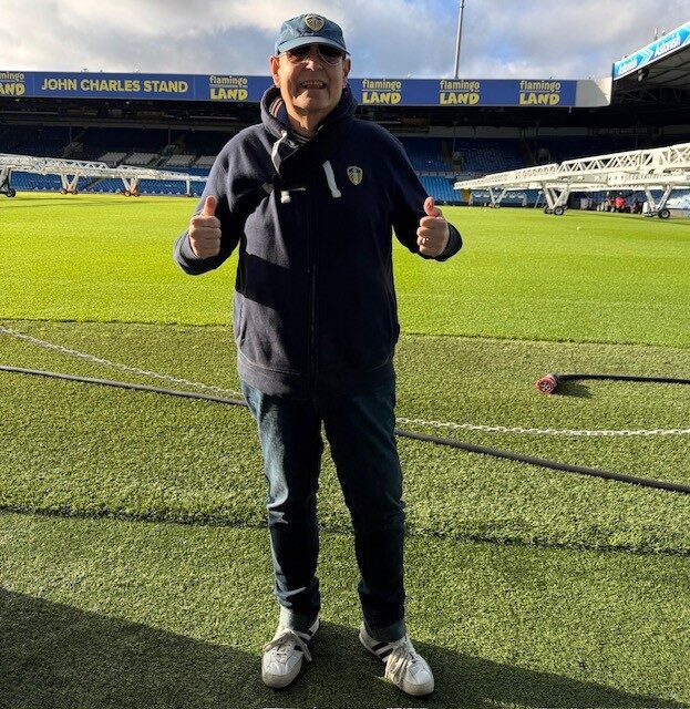 A person on the field of Elland Road Stadium giving two thumbs up to the camera.
