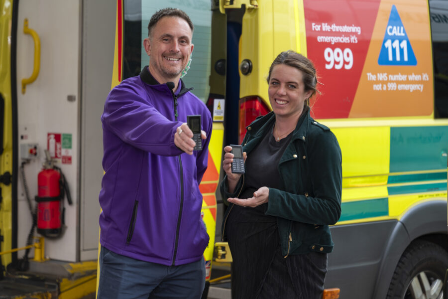 A man and a woman holding a mobile phone stood in front of an ambulance