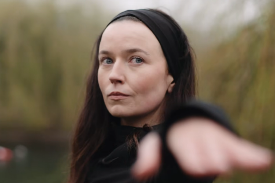 A woman with a black hairband stood outside with her arm stretched out