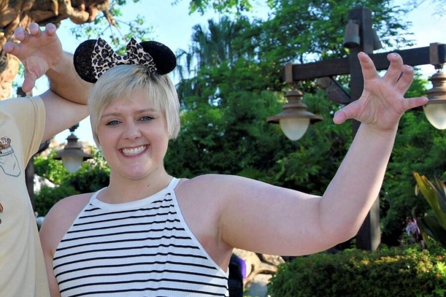 A woman in a black and white top and wearing mickey mouse ears stood beneath a leafy tree
