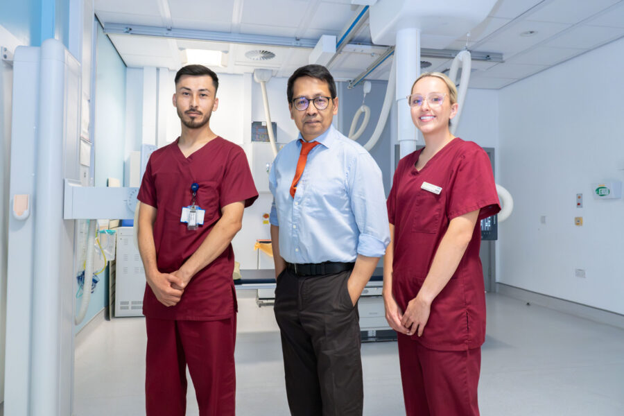 A man in a white shirt and red tie stood with two people in burgundy scrubs in a clinical space