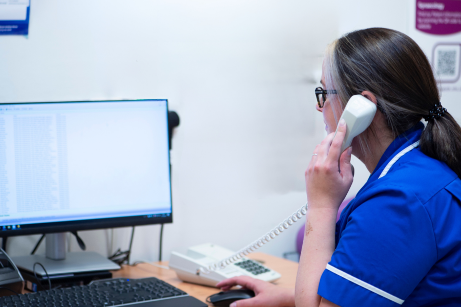 Sister in dark blue nurses uniform sat using a computer on the phone.