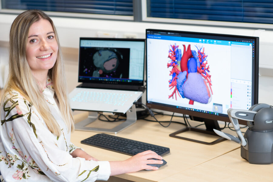 A photo of a Biomedical Engineer sat in front of a computer showing computer-aided design for creating patient 3d heart replicas.